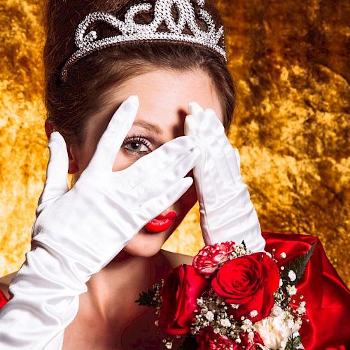 A woman wearing a tiara, white gloves, and holding roses covers her face with her hands against a gold background.