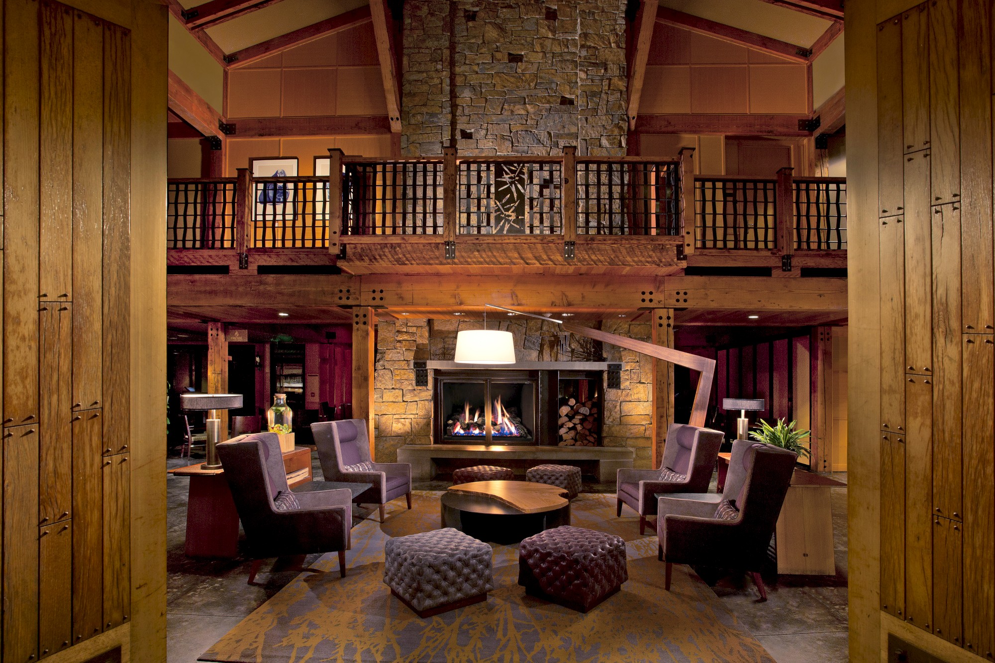 A cozy, rustic living room with a stone fireplace, wooden beams, and modern furniture arranged in a circle around a coffee table, creating a warm ambiance.