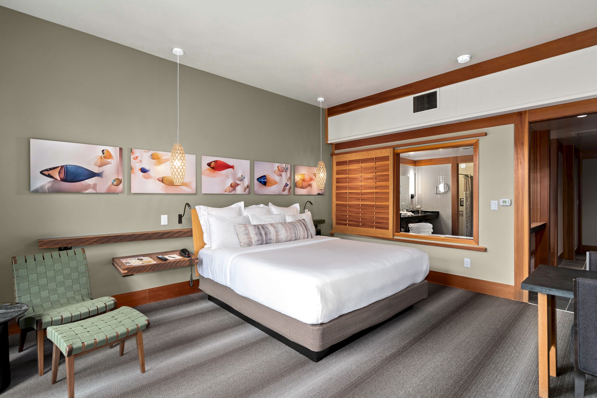 A modern bedroom features a white bed, a green chair, fish-themed wall art, a wooden accent wall, and a window opening to an adjacent room ending the sentence.