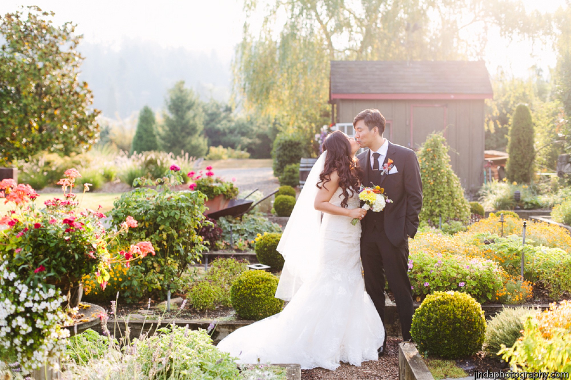 A bride and groom, in a garden setting, share an intimate moment on their wedding day surrounded by lush greenery and colorful flowers.