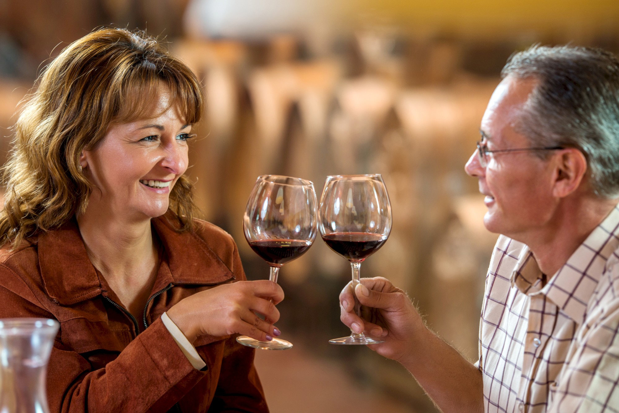 A man and a woman are clinking their red wine glasses while smiling at each other, seemingly enjoying a pleasant moment together.