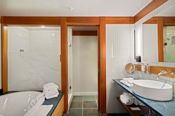 A modern bathroom features a bathtub, sink, large mirror, and ample counter space with neatly folded towels and toiletries.