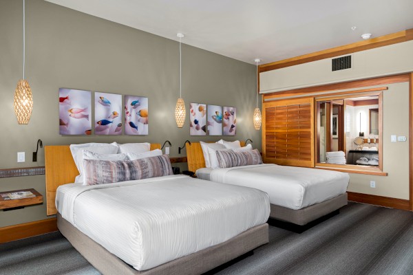 A modern hotel room with two neatly made beds, pendant lights, art above the beds, and a large mirrored closet door, creating a clean and inviting ambiance.