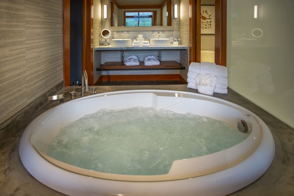 A luxurious bathroom with a bubble-filled circular bathtub, folded towels, and a modern double-sink vanity in the background.