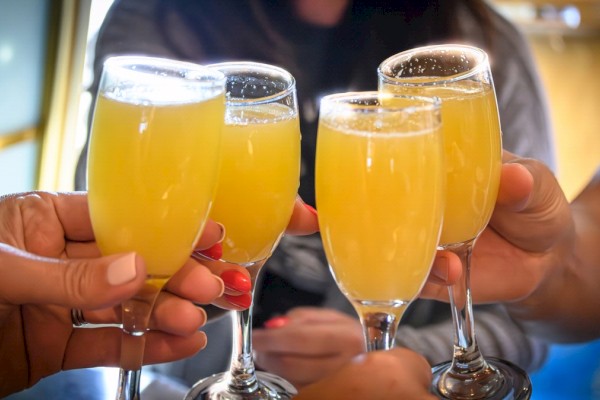 Four people clinking glasses filled with a yellow drink, likely mimosas, in a celebratory gesture.