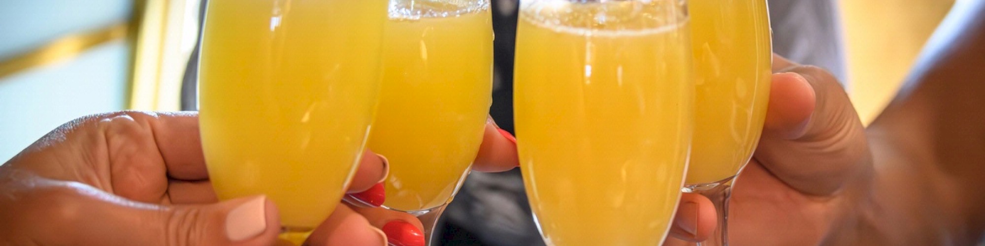 Four people are clinking glasses filled with a yellow beverage, possibly mimosas, in a celebratory gesture.