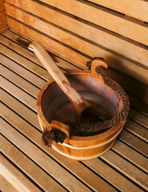 A wooden sauna bucket and ladle on a wooden bench, typical in a sauna setting.