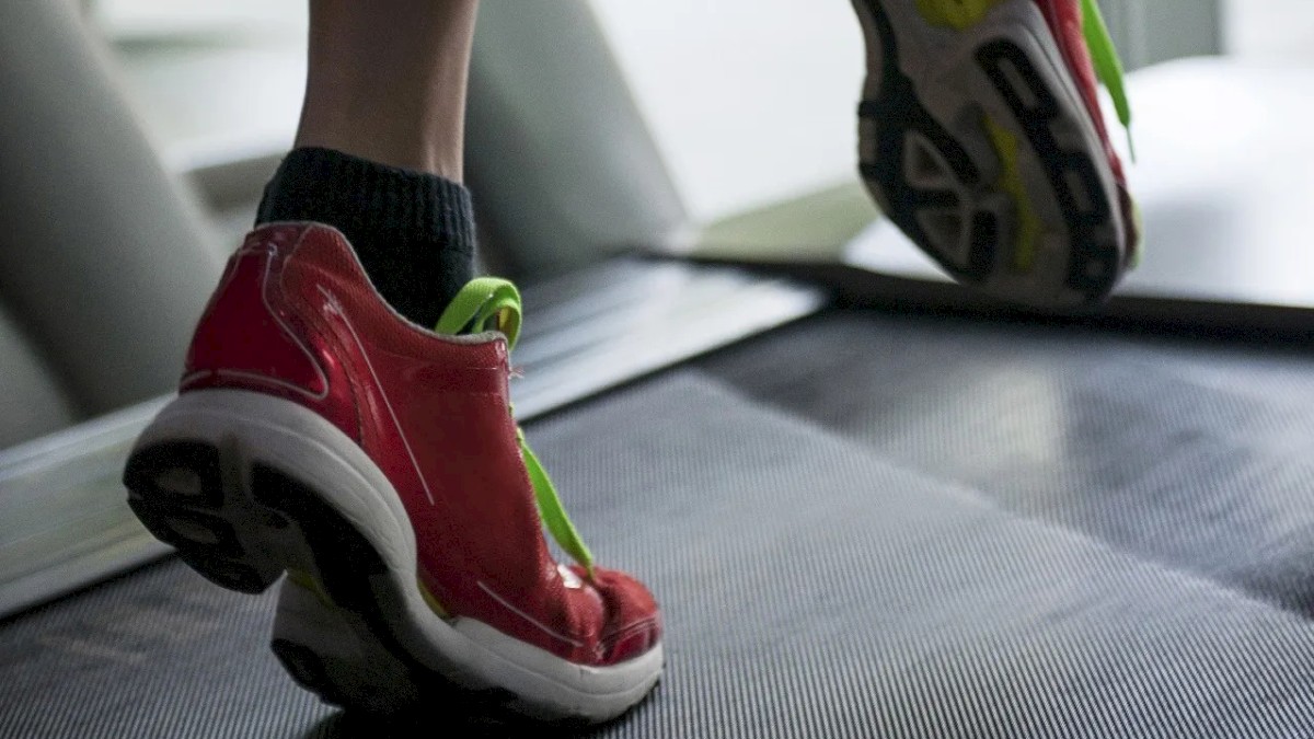 The image shows a person wearing red athletic shoes running on a treadmill, illustrating a moment of indoor exercise.