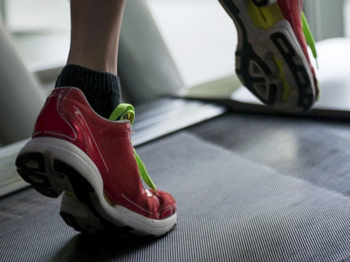 The image shows a person wearing red athletic shoes running on a treadmill, illustrating a moment of indoor exercise.