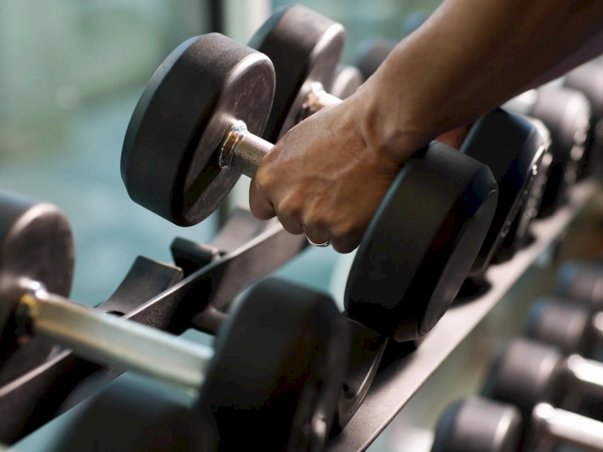 A person is picking up a dumbbell from a rack in a gym, with multiple other dumbbells visible in the image.