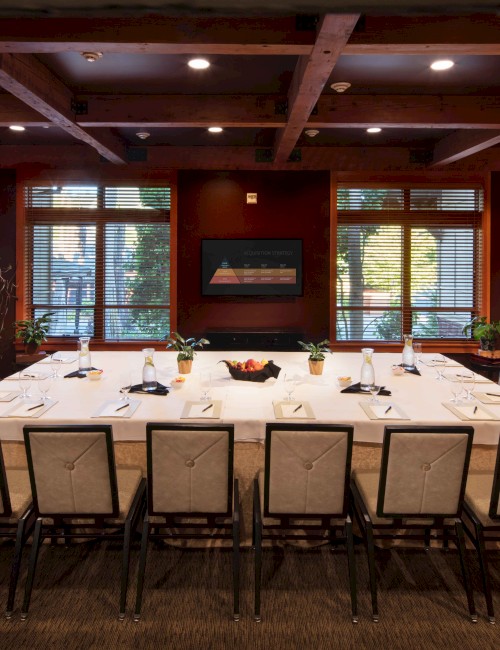 A conference room with a rectangular table set for a meeting, surrounded by chairs, with a fireplace and bookshelves on the right side of the room.