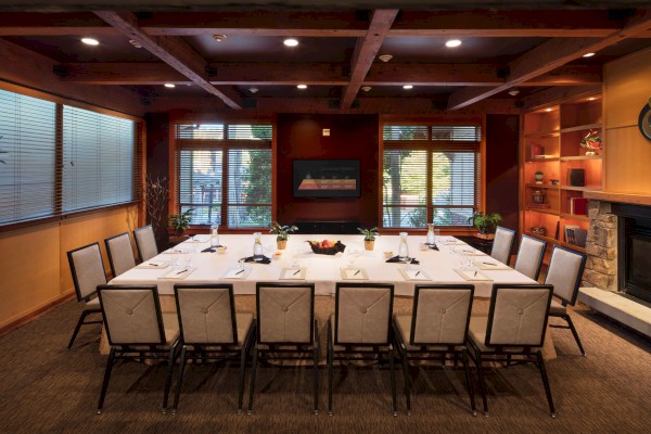 A conference room with a U-shaped table, chairs, and a fireplace; windows and shelves line the walls, offering a cozy atmosphere.