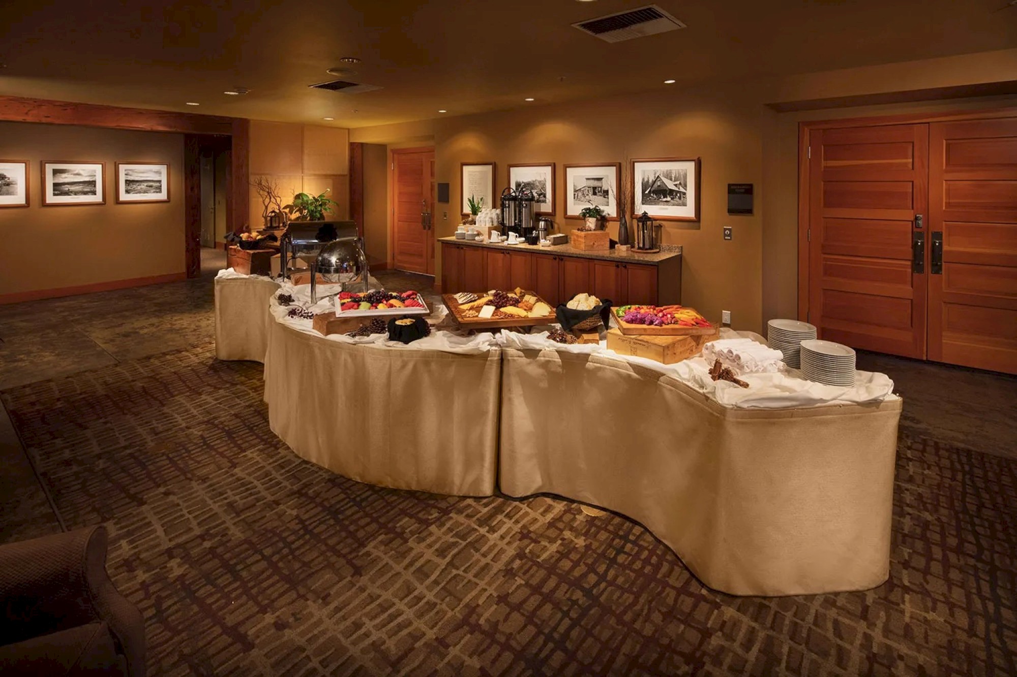 A room with a buffet table set up with various foods and drinks, with framed photos on the walls and wooden doors in the background.