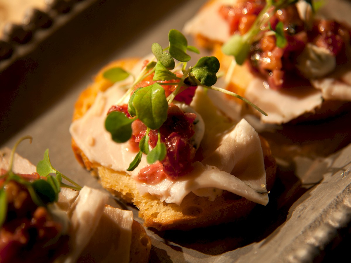 The image shows a tray of gourmet appetizers made of toasted bread topped with sliced meat, a dollop of sauce, and garnished with microgreens.