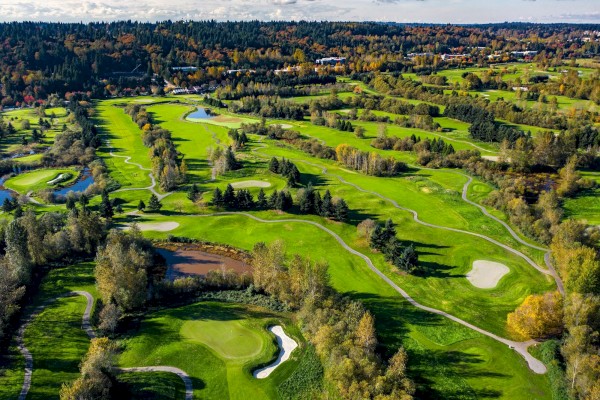 An aerial view of a golf course with multiple fairways, greens, sand traps, and winding paths surrounded by trees and water features.