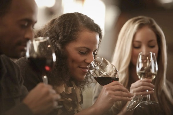 Three people are engaged in a wine tasting, each holding a wine glass and smelling the wine's aroma before drinking.