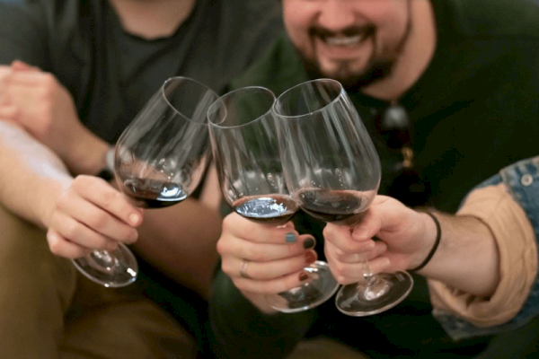 Four people clink glasses of red wine, smiling and celebrating together.