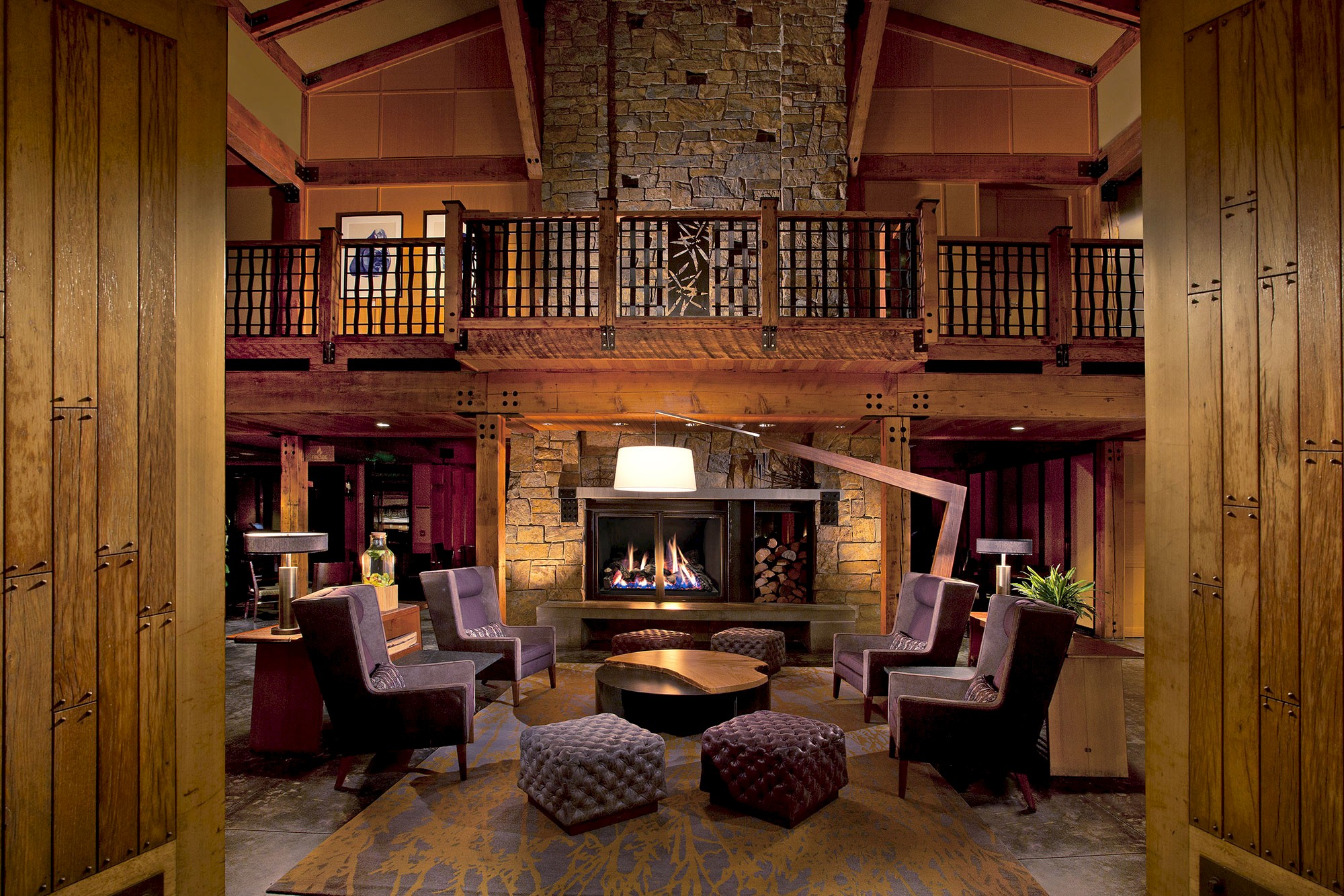 This image shows a cozy, well-appointed lodge interior with a fireplace, comfortable seating, wooden accents, and warm lighting, creating a welcoming atmosphere.