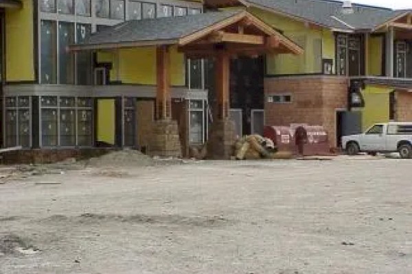 The image shows a building under construction with yellow walls and large windows. A white vehicle and some construction materials are visible.