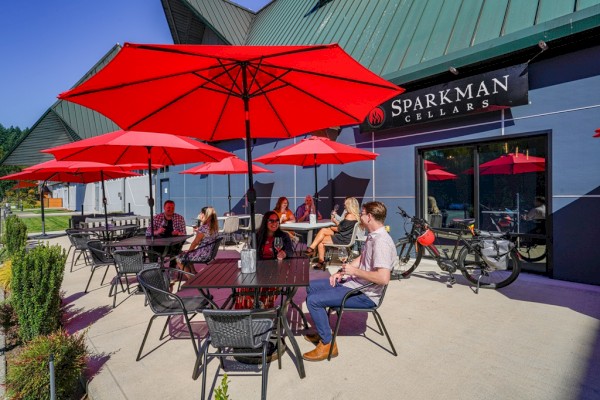 People sitting and talking at an outdoor seating area of a place called Sparkman Cellars with red umbrellas and modern outdoor furniture.