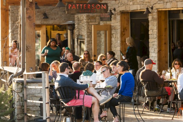 People are dining and socializing at an outdoor restaurant named Patterson, enjoying food and drinks in a lively atmosphere, ending the sentence.