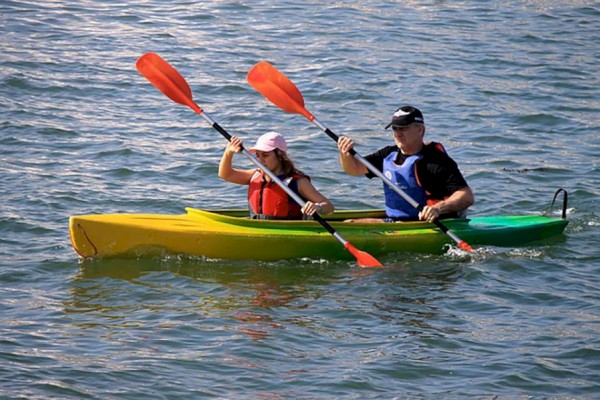 Two people are kayaking on a body of water, each holding a double-bladed paddle and wearing life jackets for safety.