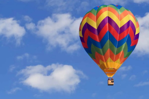 A colorful hot air balloon floats against a bright blue sky with scattered white clouds.