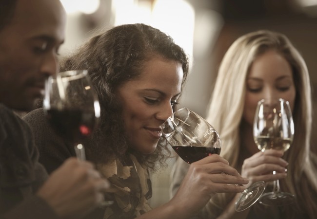 Three people are enjoying and sniffing glasses of wine in a relaxed, social setting.