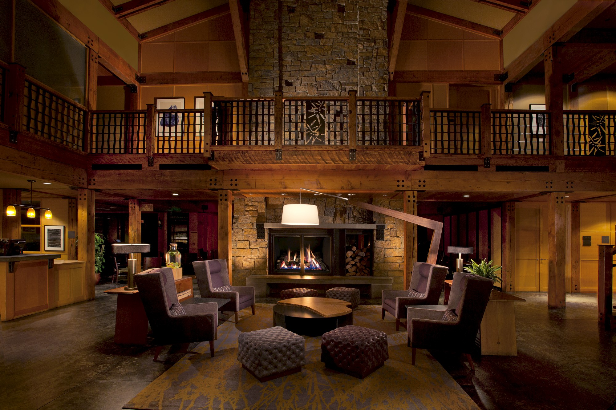 A cozy lobby with a fireplace, modern furniture, and warm lighting, surrounded by wooden accents and a high ceiling.