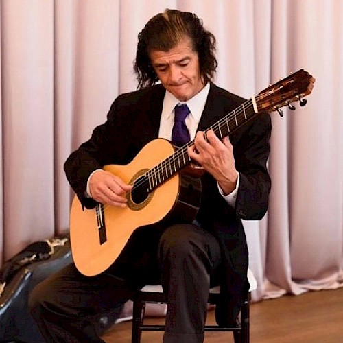 Classical Guitarist Patricio Contreras Playing his Guitar in front of a Pink Curtain