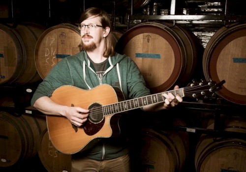 Ian Hale Skavdahl playing a guitar in front of wine barrels