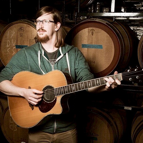 Ian Hale Skavdahl playing a guitar in front of wine barrels