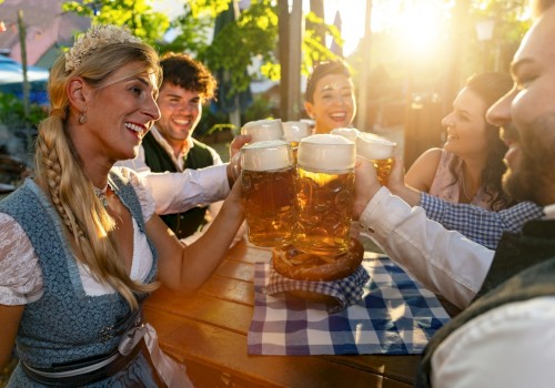 A group of people are enjoying a sunny outdoor gathering, toasting with large mugs of beer, with one woman dressed in traditional attire.