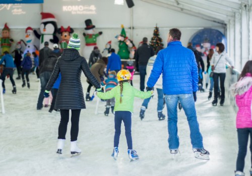 People are ice skating at an indoor rink, holding hands, while festive decorations adorn the background.