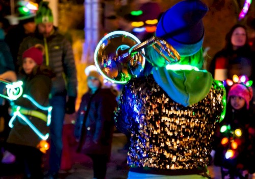 A person with glowing attire plays a trumpet outdoors, surrounded by a crowd in colorful, illuminated outfits.