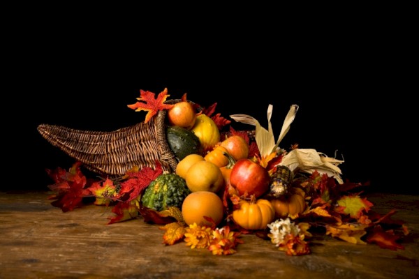 A cornucopia filled with pumpkins, gourds, and leaves arranged on a wooden surface, representing an autumn harvest setting.