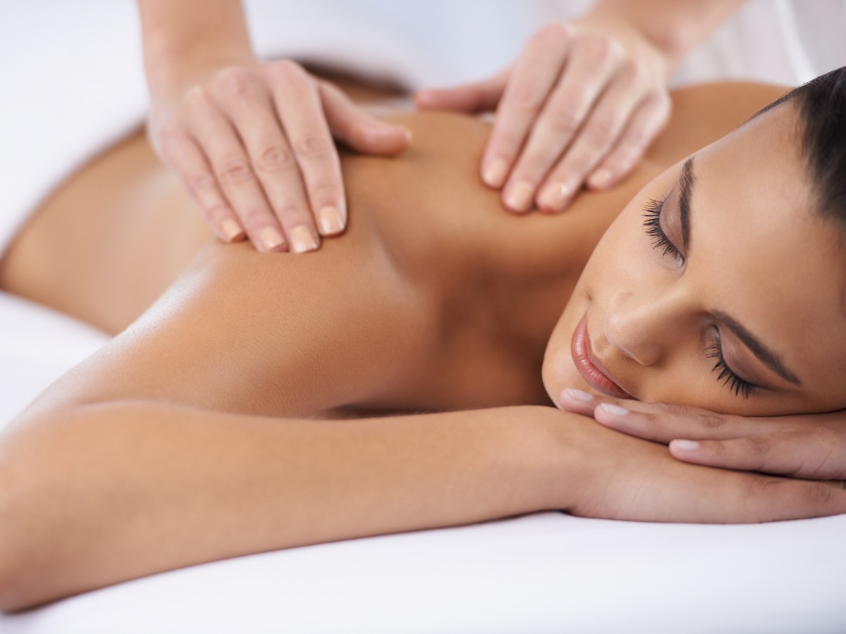 A person receiving a back massage, lying face down on a massage table with eyes closed, appearing relaxed and peaceful.