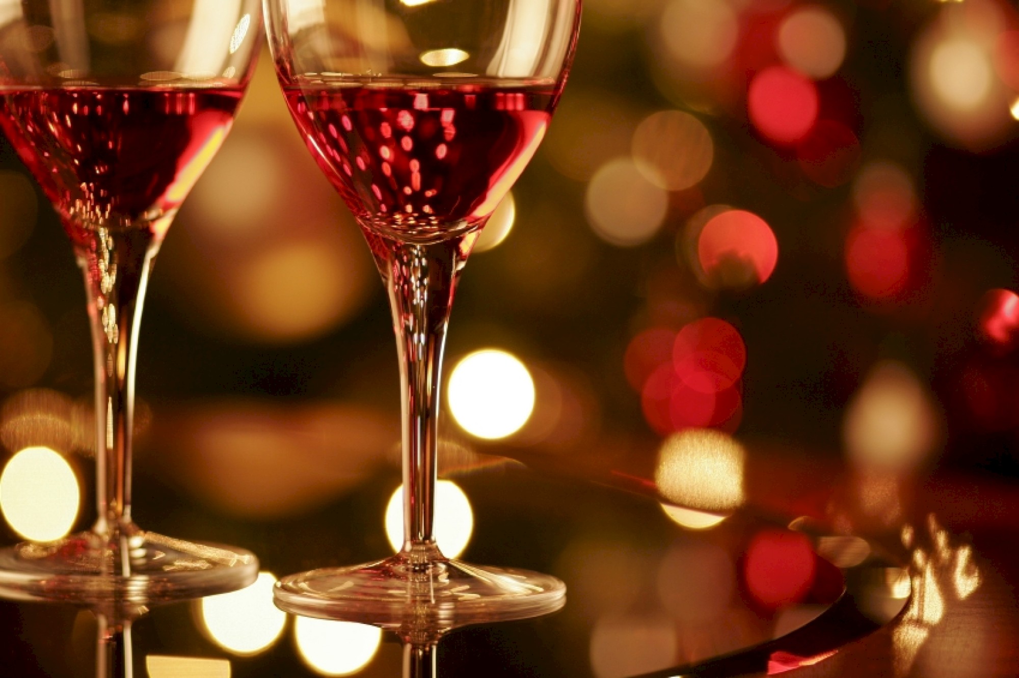 Two glasses of red wine on a table with a blurred background of festive, warm lights.