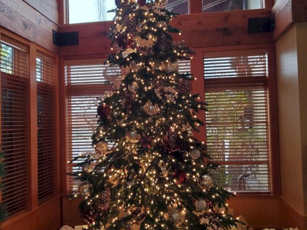 A decorated Christmas tree with lights and ornaments, surrounded by wrapped gifts, stands in a cozy room with wooden accents.