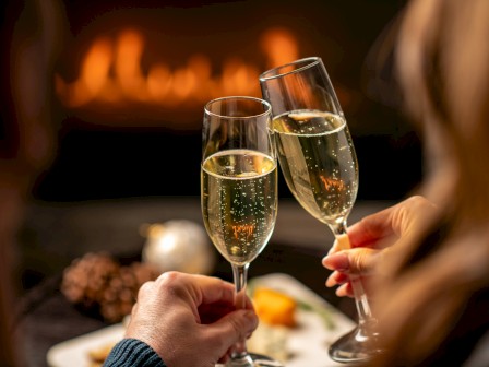 Two people clinking champagne glasses in a cozy setting with a warm glow in the background.