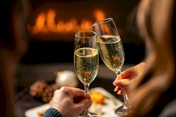 Two people clinking champagne glasses in a cozy setting with warm lighting and a blurred background.