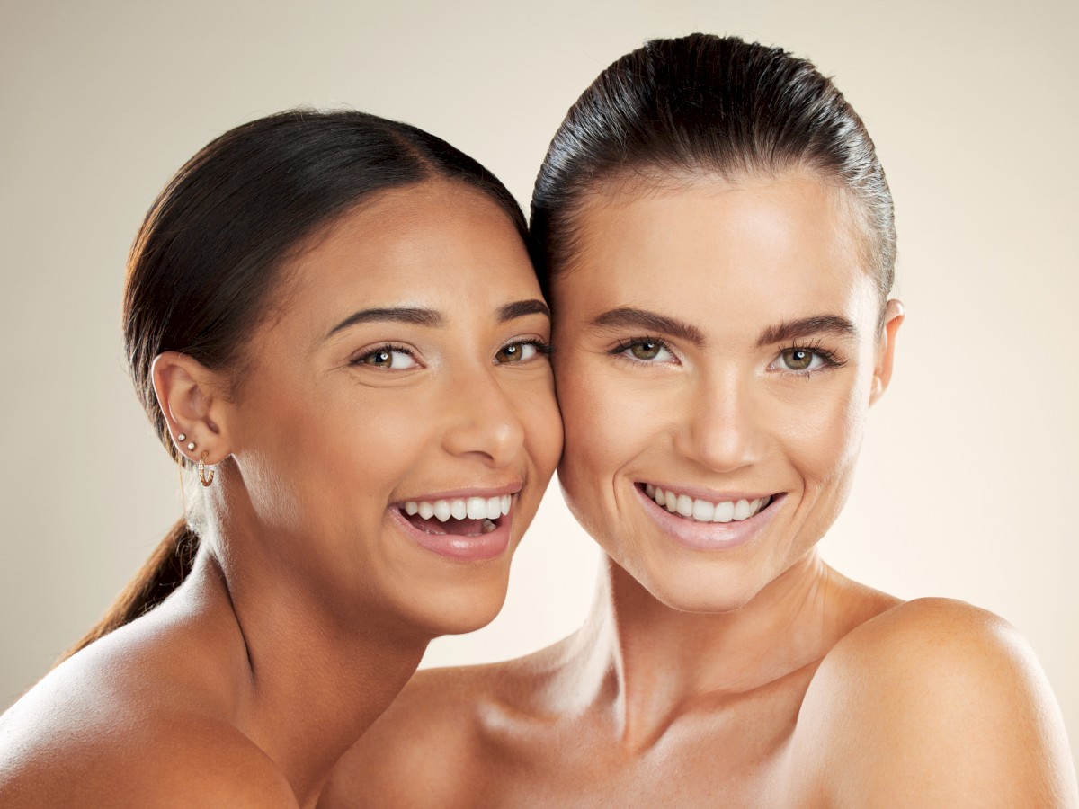 Two people are smiling and posing closely together against a neutral background.