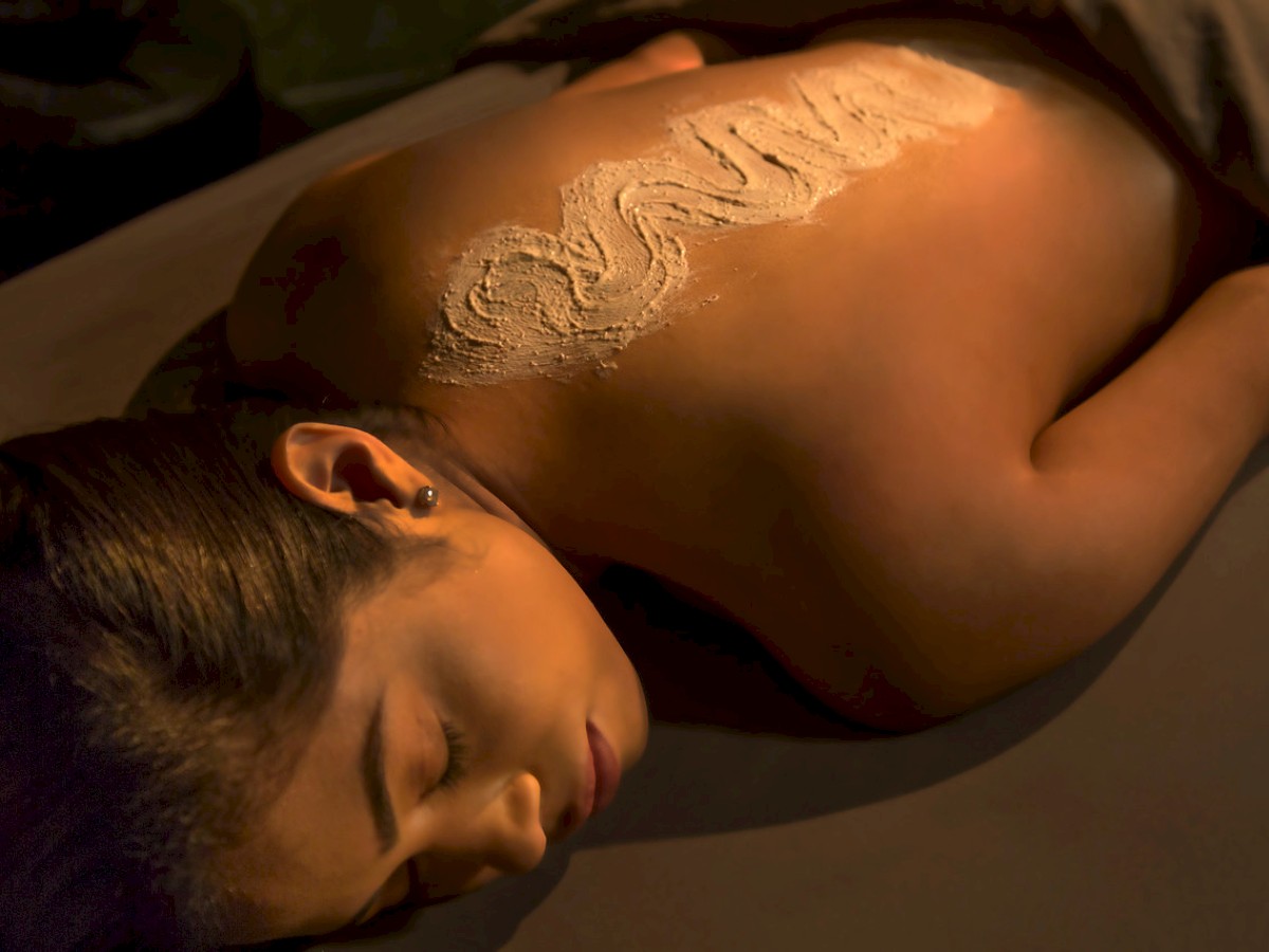 A person is lying face down, receiving a treatment with a substance applied to their back, in a relaxing environment.